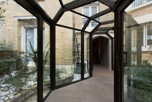 A glass-enclosed corridor with a view of a brick building and a garden with rocks and plants. - Hôtel Beaugrenelle Saint Charles (Paris)