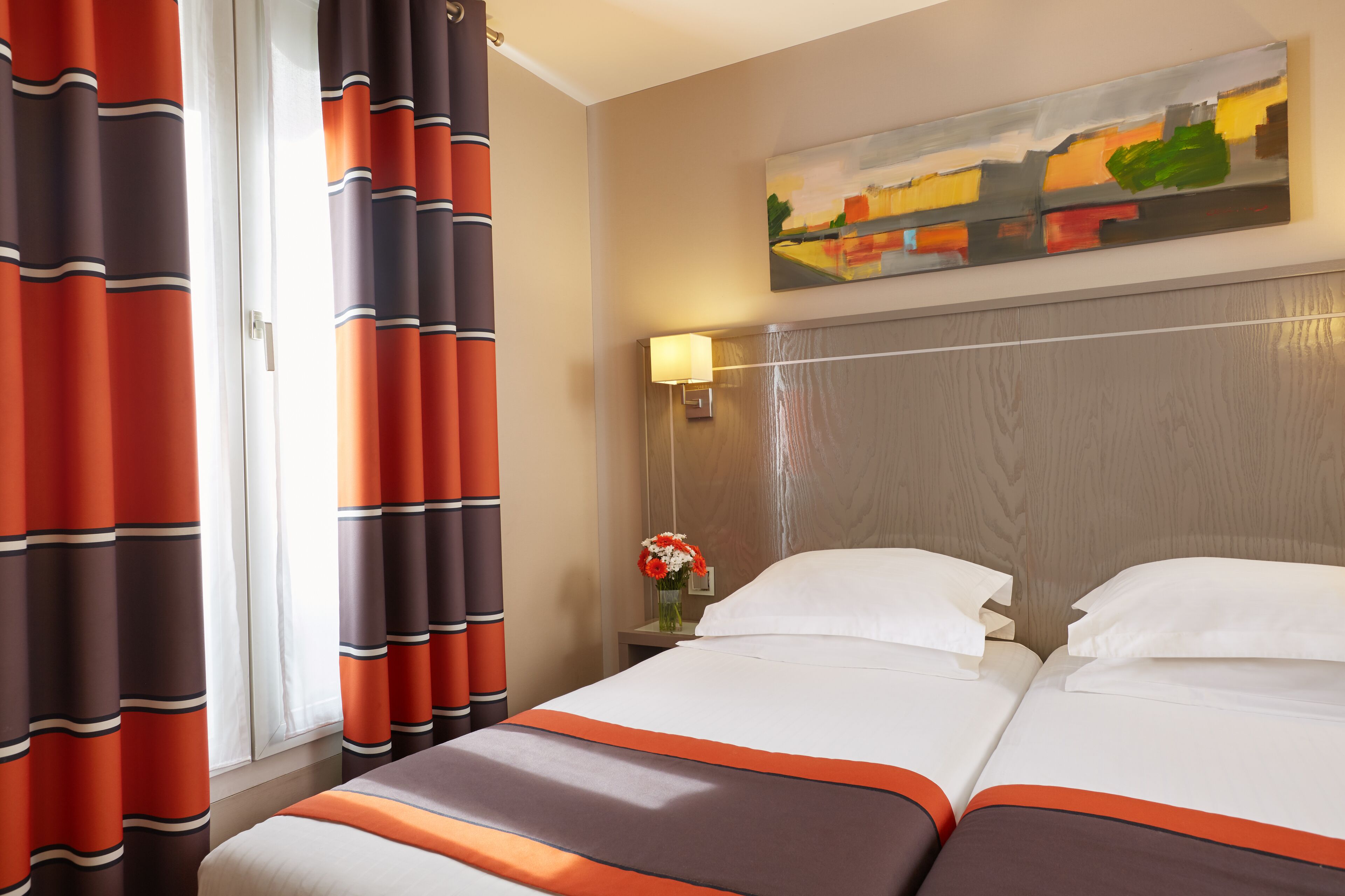 Habitación de hotel con dos camas, un cuadro en la pared, una mesita de noche con lámpara y cortinas.