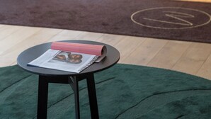 A reception area with a reception desk, a green carpet, and a small table with a magazine. - Makom Pereire (Paris)