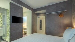 A modern hotel room with a large bed, a flat-screen TV mounted on the wall, and a walk-in closet with a mirror. - Makom Pereire (Paris)