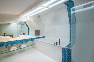 A modern bathroom with a large bathtub, two sinks, and a glass-enclosed shower area.