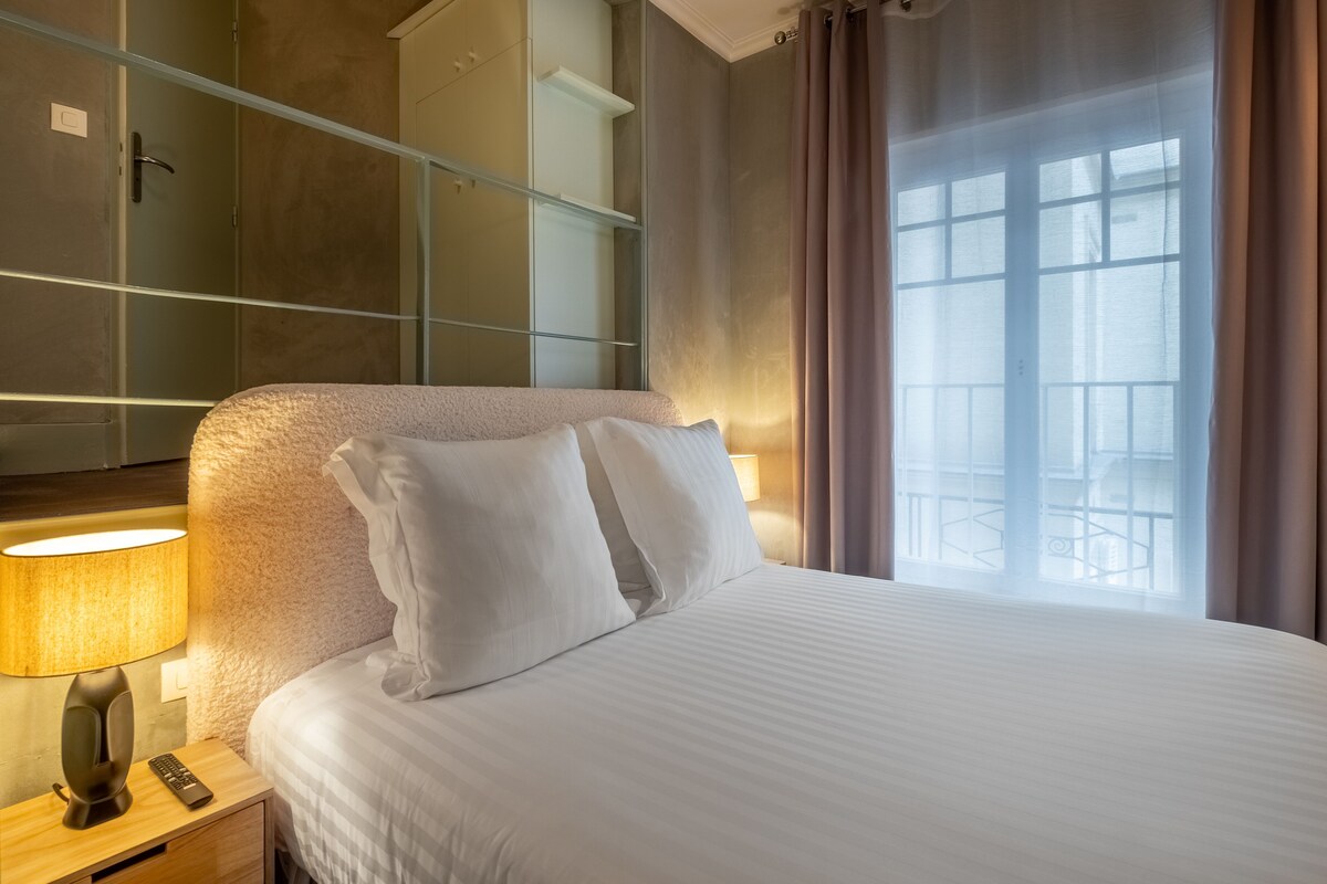A hotel room with a bed, bedside lamp, and a view of the outside.
