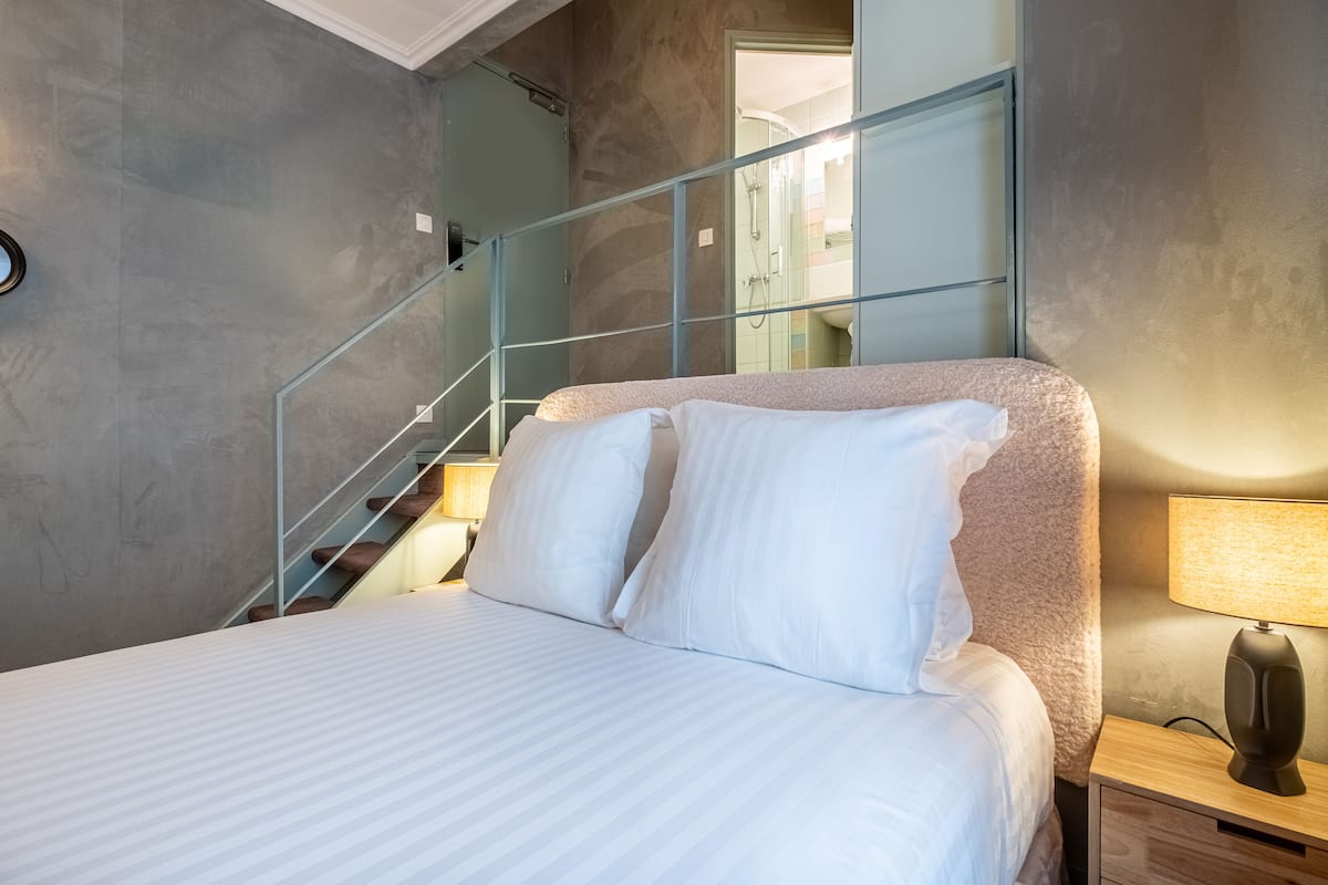 Quarto de hotel moderno com uma cama grande, escada de vidro e vista para o banheiro.