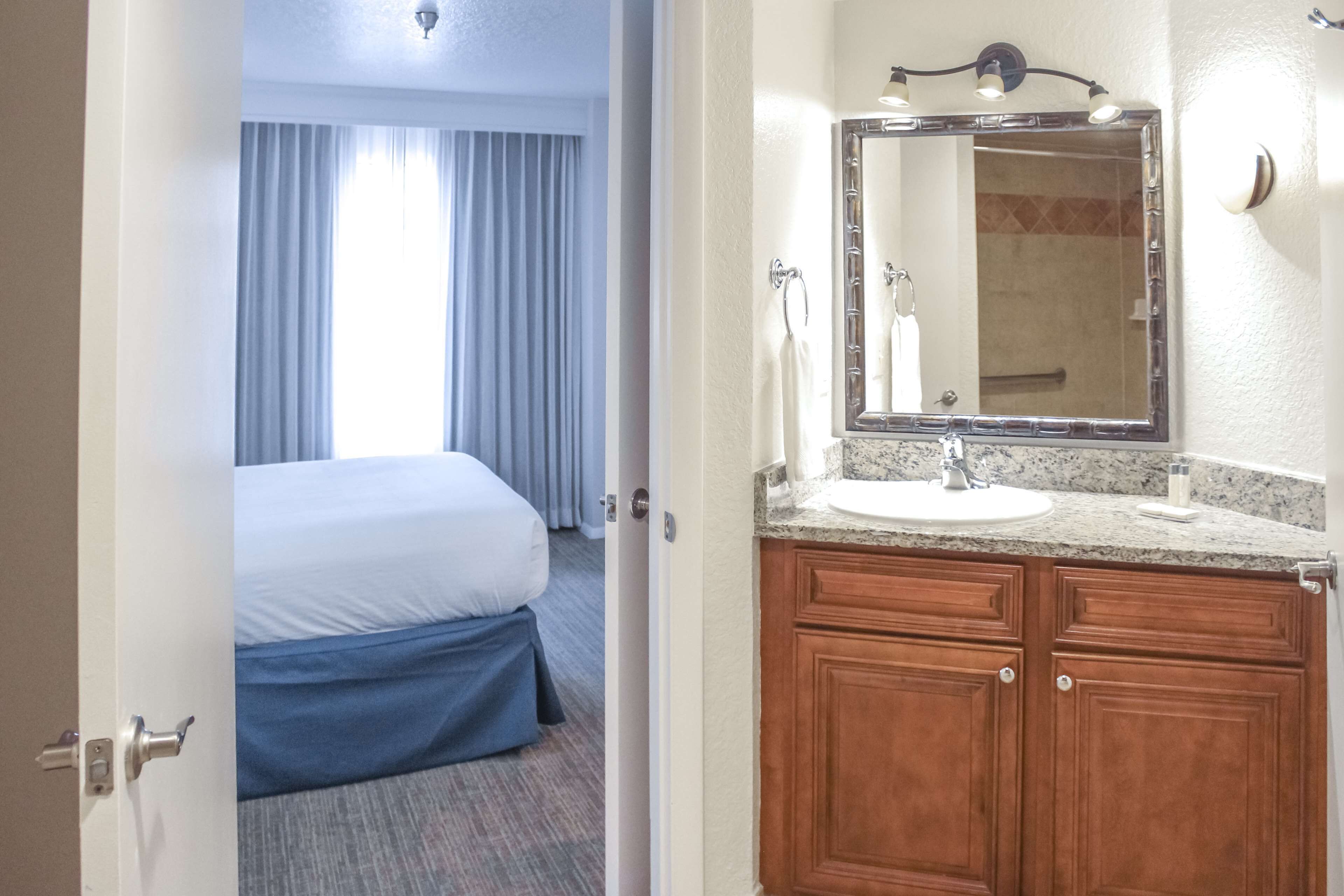 A hotel room with a bed, a bathroom with a sink and mirror, and a door leading to another room.