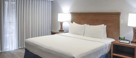 Una habitación de hotel con una cama grande, dos mesitas de noche, una lámpara y un ventanal con cortinas.