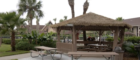 A gazebo with picnic tables, surrounded by palm trees and a well-maintained lawn.