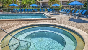 A swimming pool with lounge chairs and umbrellas, surrounded by a brick patio. - Hilton Vacation Club Polynesian Isles Kissimmee (Kissimmee)