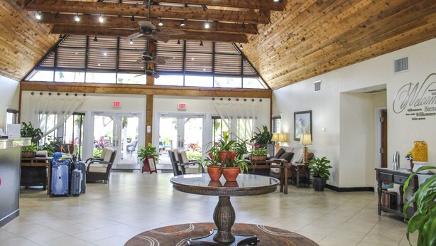 A spacious lobby with a high ceiling, wooden beams, and a central round table surrounded by chairs. There are potted plants, a reception desk, and a wall with a welcome sign. - Hilton Vacation Club Polynesian Isles Kissimmee (Kissimmee)