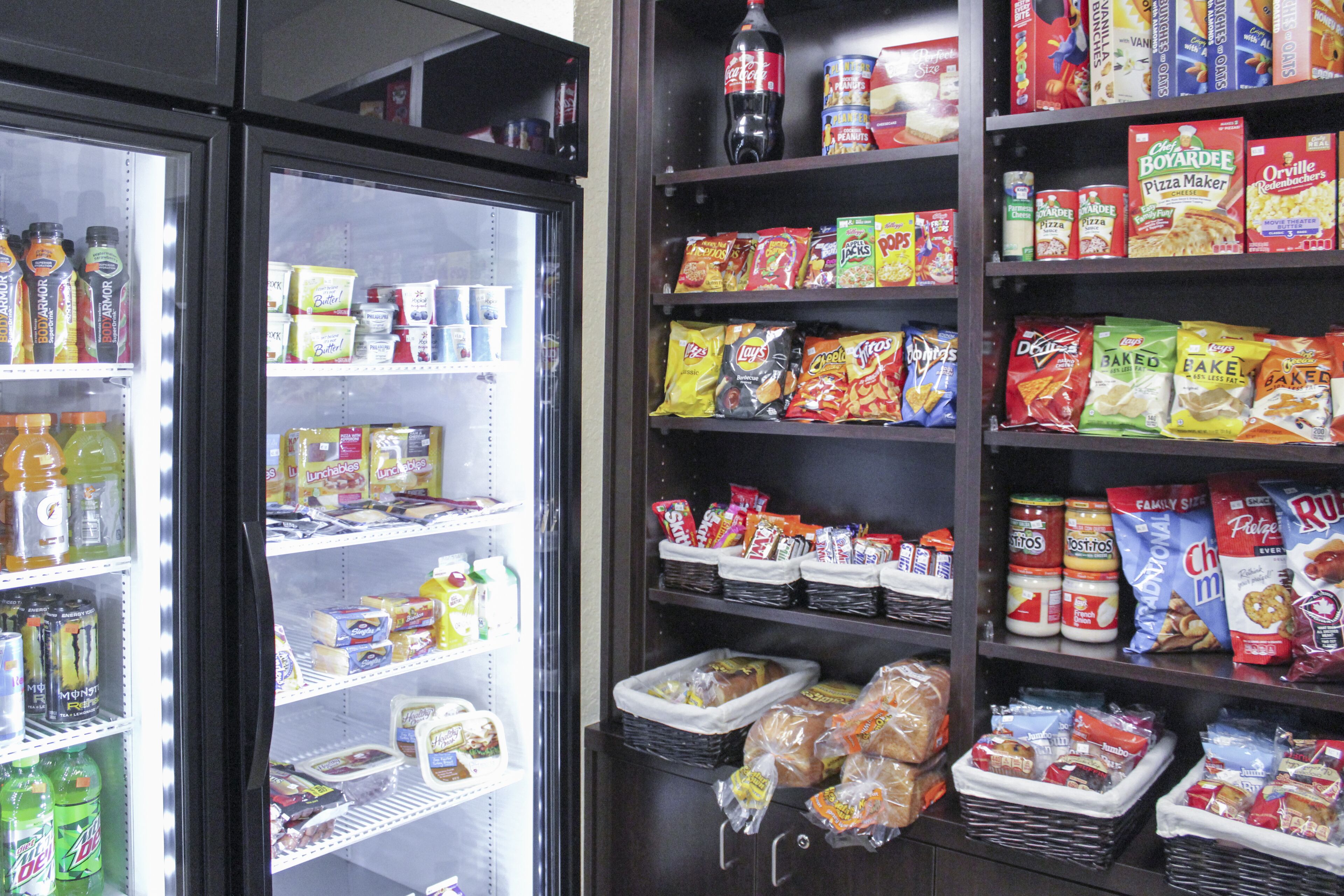 A refrigerated section with various beverages and a shelf stocked with snacks and packaged foods.
