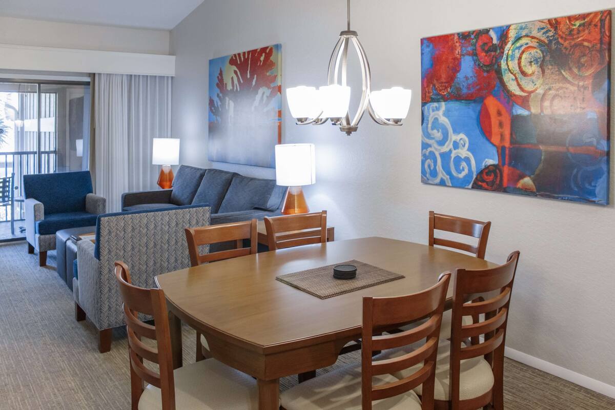 A hotel room with a dining area, a sofa set, and two paintings on the wall.