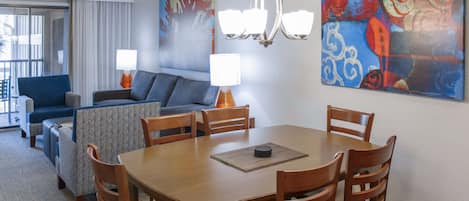 A hotel room with a dining area, a sofa set, and two paintings on the wall.