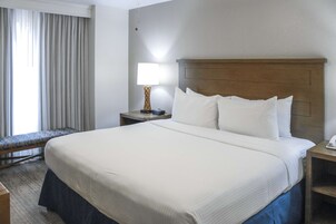 Hotellihuone, jossa on suuri sänky, yöpöytä lampun kanssa, penkki ikkunan vieressä ja näkymä ulos.