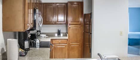A kitchen with wooden cabinets, a stainless steel sink, a coffee maker, and a refrigerator.