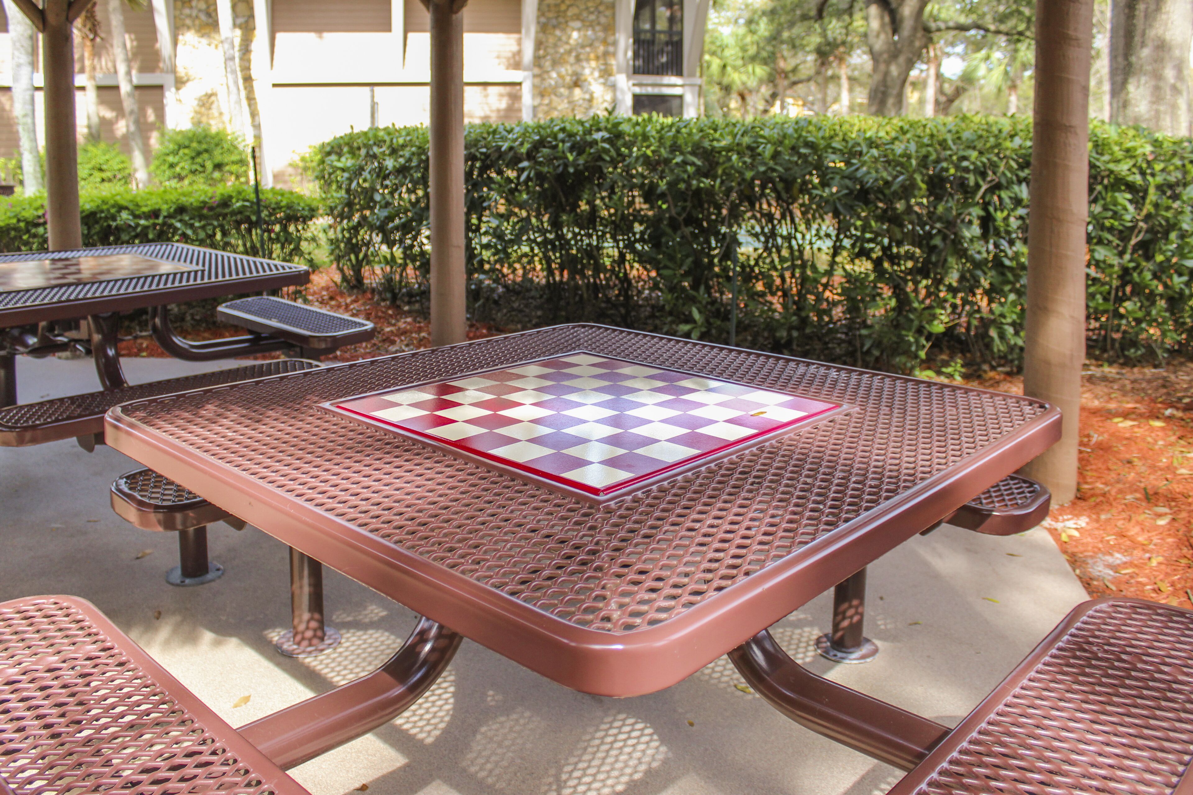 Una mesa de picnic metálica con mantel a cuadros, rodeada de follaje y árboles.