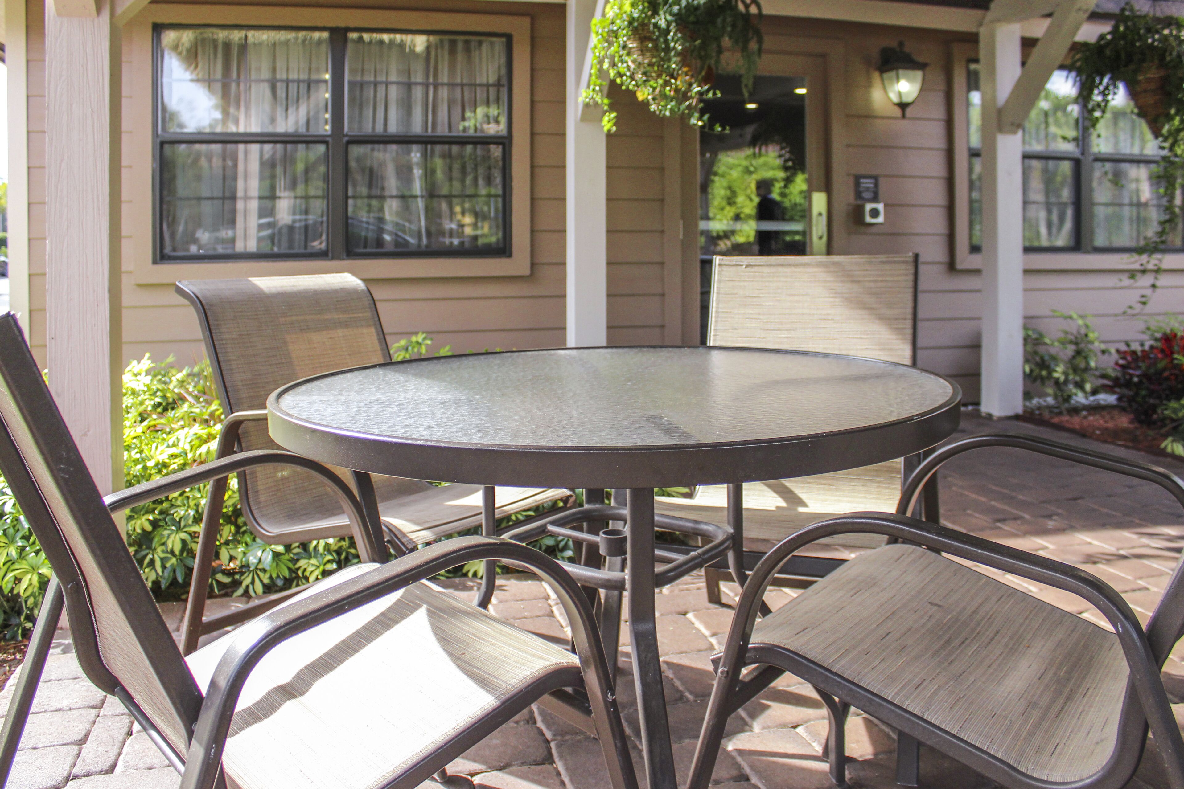 A round metal table with four chairs, set on a brick patio with a house in the background.