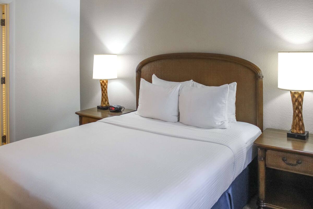 A neatly made bed with white linens, two bedside tables with lamps, and a wooden headboard.