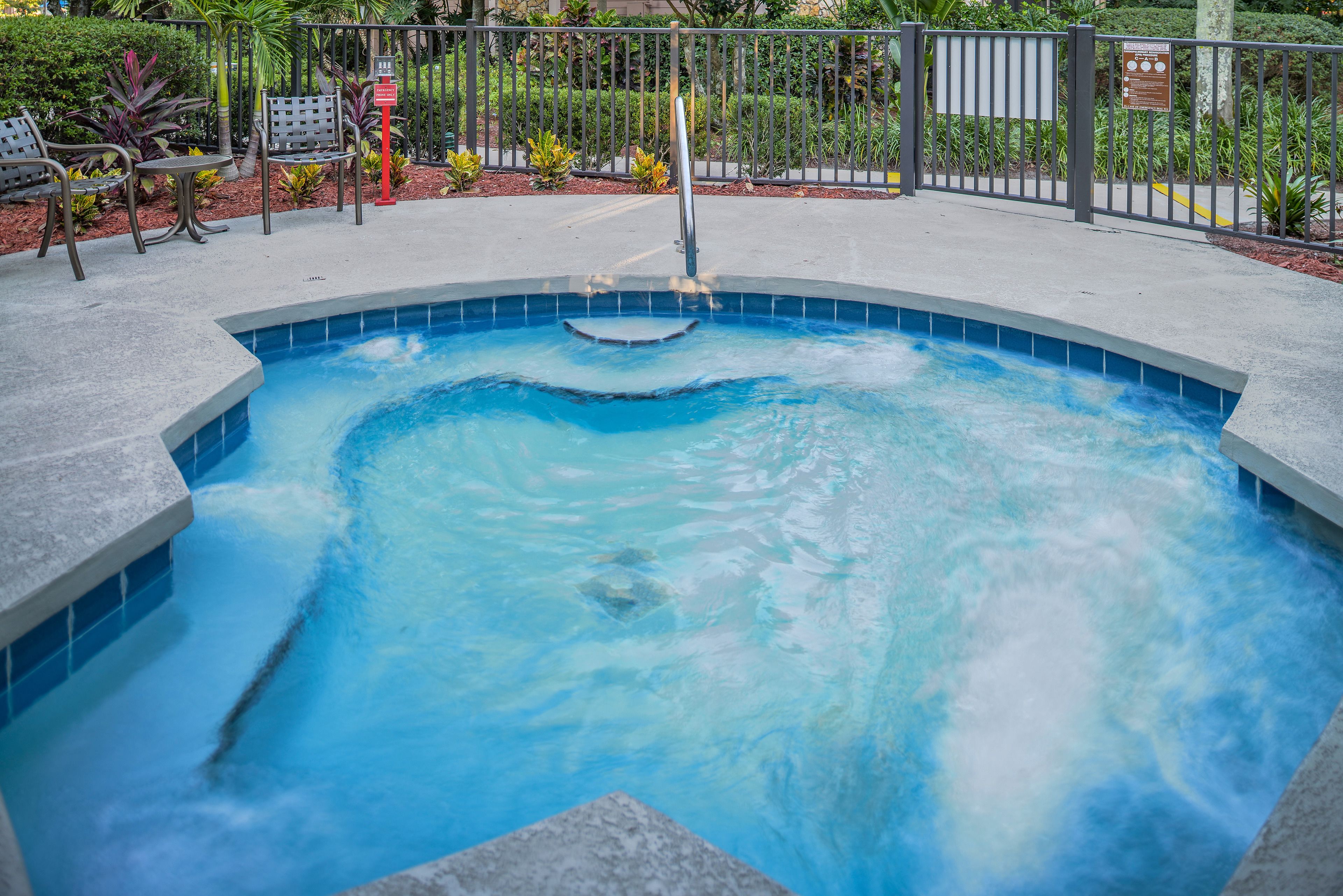 Una vasca idromassaggio con ringhiera metallica e area piscina con sedie e piante.