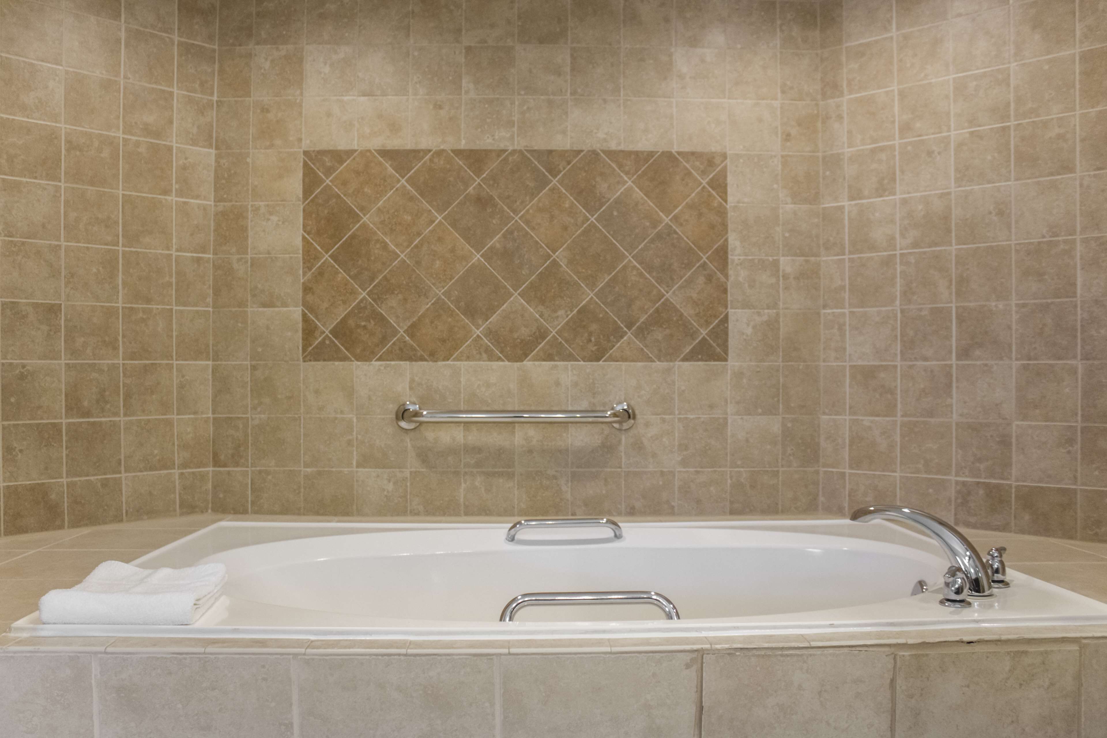 A bathroom with a large bathtub, a towel rack, and a decorative tile wall.
