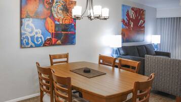 Un comedor con una mesa y sillas de madera, una araña y dos cuadros en la pared.