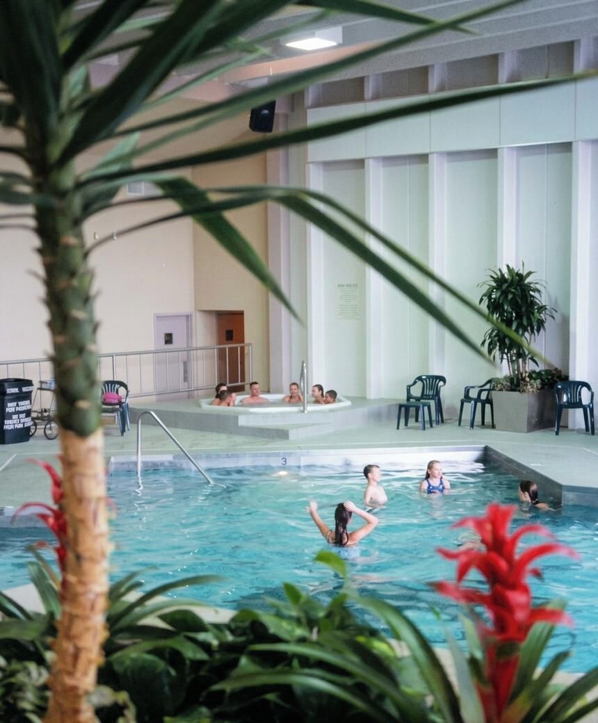 Piscina interior con varias pistas, rodeada de sillas y plantas en macetas.
