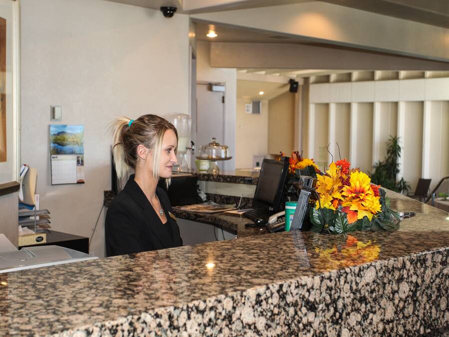 A reception desk with a granite countertop, a computer, and a vase of flowers.