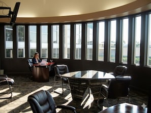A conference room with a large oval table, several chairs, and a person working at a desk. - The Greenwell Inn (Price)