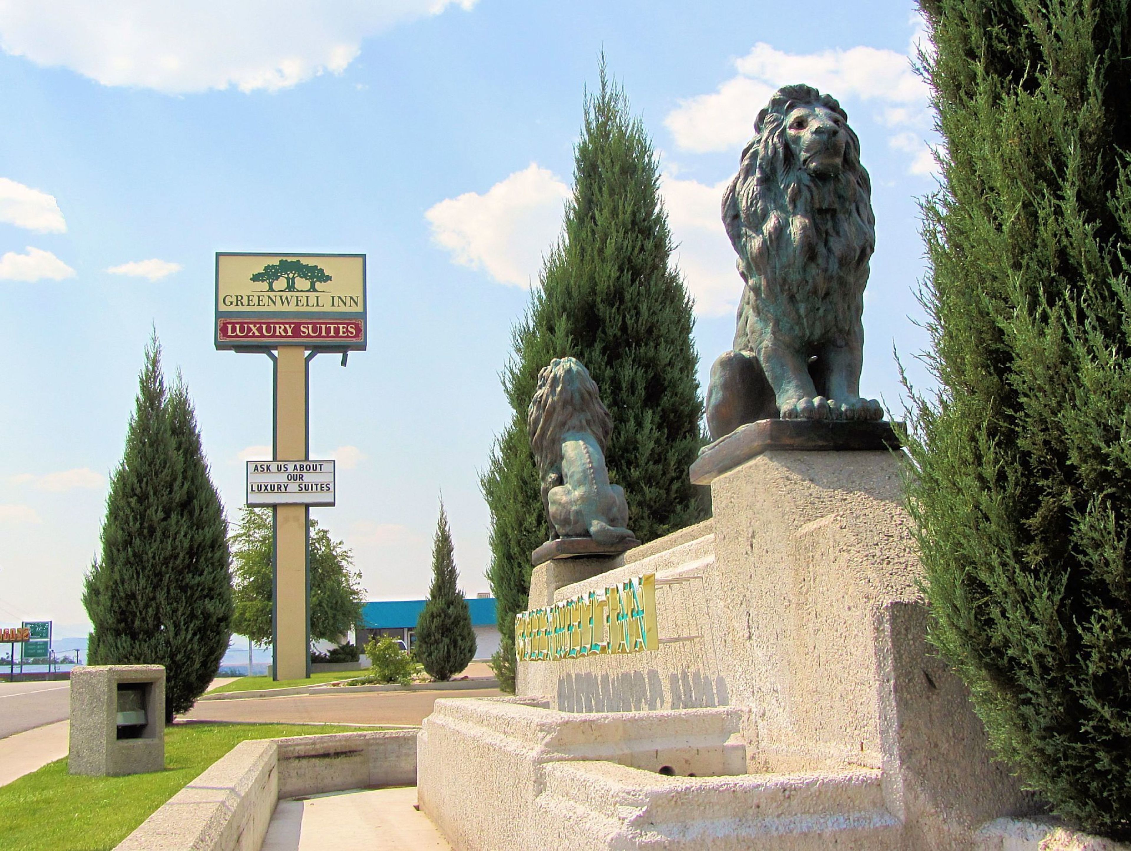 Señal de Greenwood Inn con suites de lujo, dos estatuas de leones y cielo despejado.