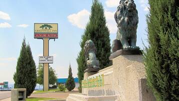 Señal de Greenwood Inn con suites de lujo, dos estatuas de leones y cielo despejado.