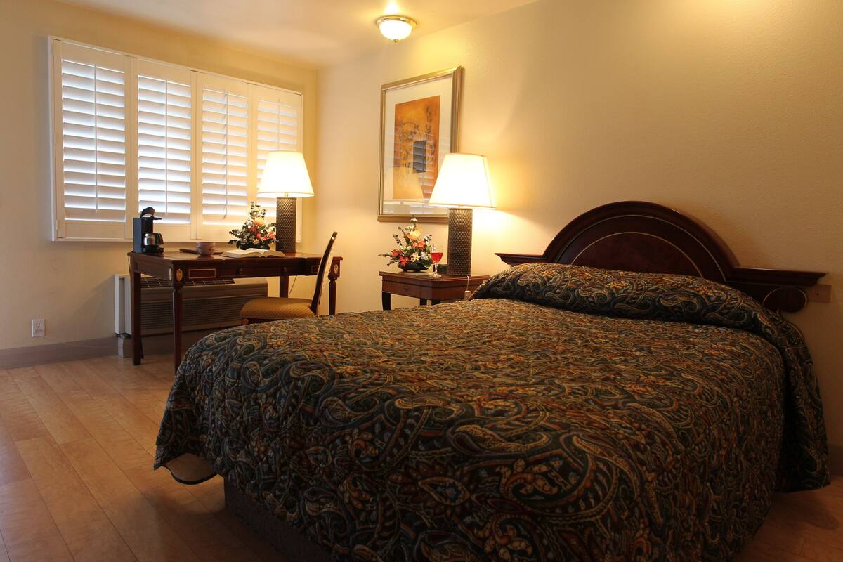 A bedroom with a large bed, a desk with a lamp, and a chair.