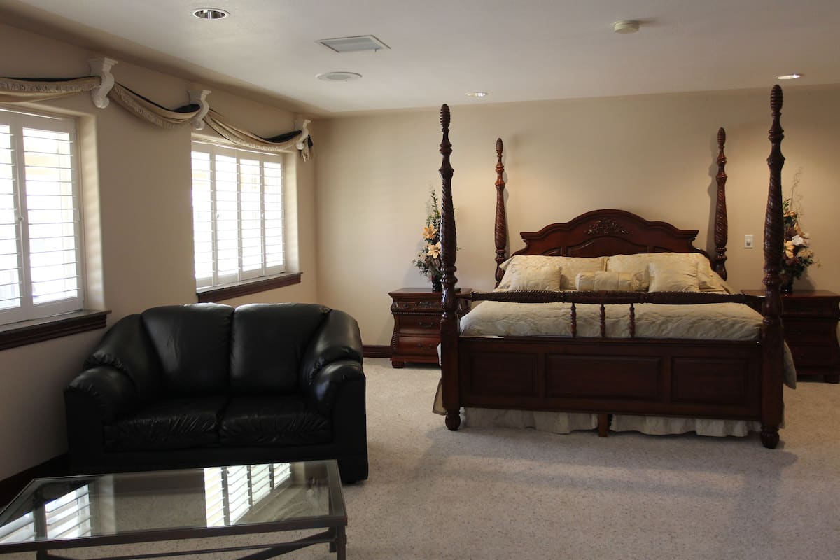 A bedroom with a four-poster bed, a leather armchair, and a glass coffee table.