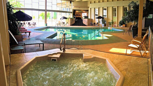 An indoor swimming pool with a hot tub, surrounded by lounge chairs and umbrellas. - The Greenwell Inn (Price)