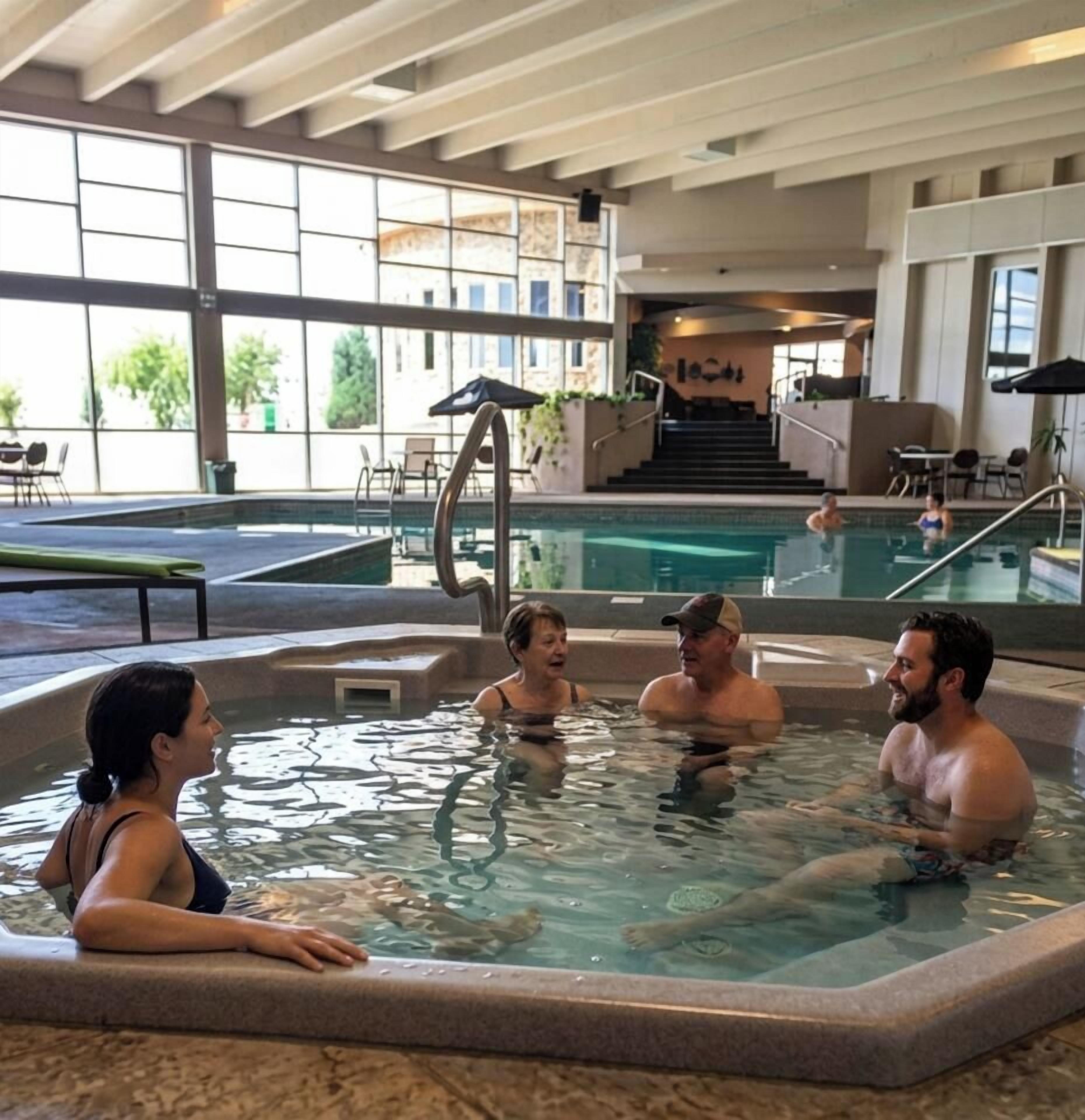 An indoor swimming pool area with clear glass walls, a separate hot tub section, and a staircase leading to an upper level.