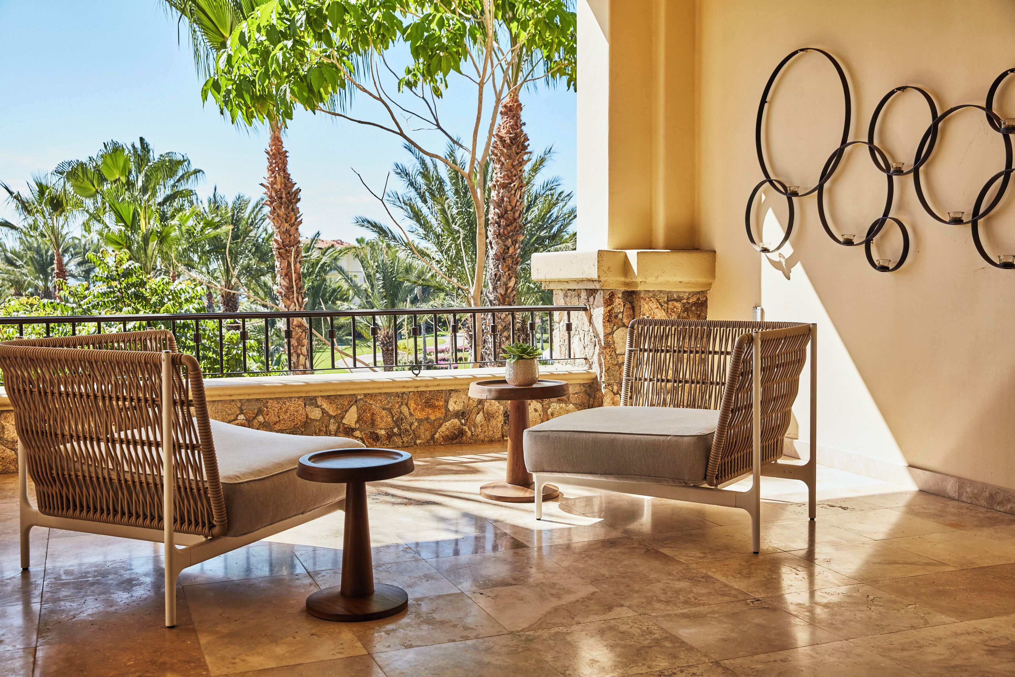 A balcony with wicker furniture, a stone wall, and a view of palm trees.