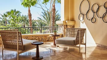 A balcony with wicker furniture, a stone wall, and a view of palm trees.