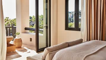 A hotel room with a balcony, a sofa, a small table with a plant, and a view of palm trees and buildings.