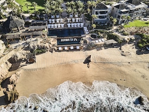 An aerial view of a resort with a swimming pool, lounge areas, and a beachfront.