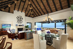 A spacious living room with a high ceiling, a fireplace, and a large window overlooking the ocean.