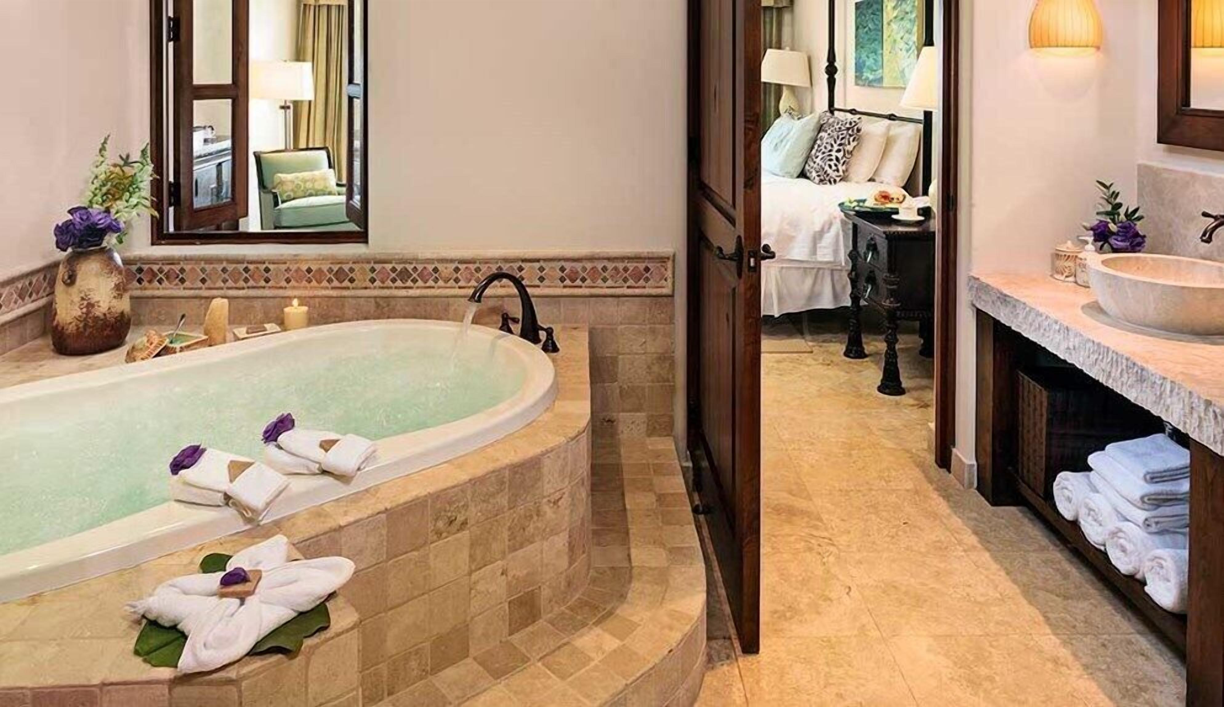 Un baño con una bañera independiente, un tocador con un lavamanos grande y una cama con una mesita de noche.