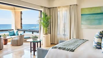 A hotel room with a balcony, a bed, a seating area with a plant, and a view of the ocean.