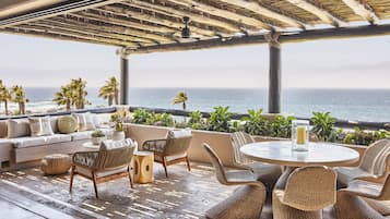 A coastal terrace with a sofa, wicker chairs, a round table, and potted plants.