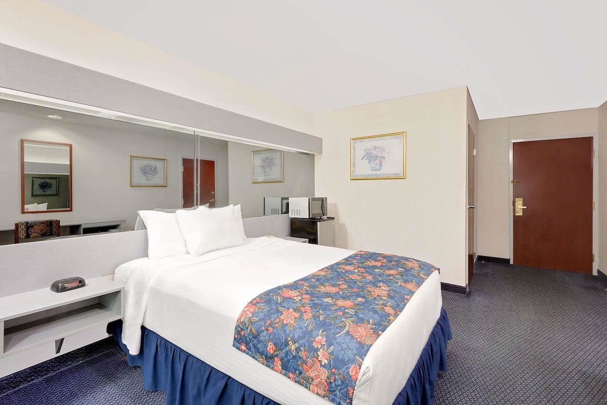 Una habitación de hotel con cama, escritorio, espejo y puerta.