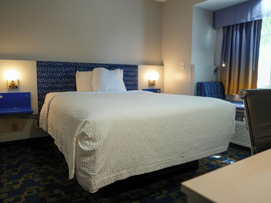 A hotel room with a large bed, two bedside lamps, a desk, and a chair.