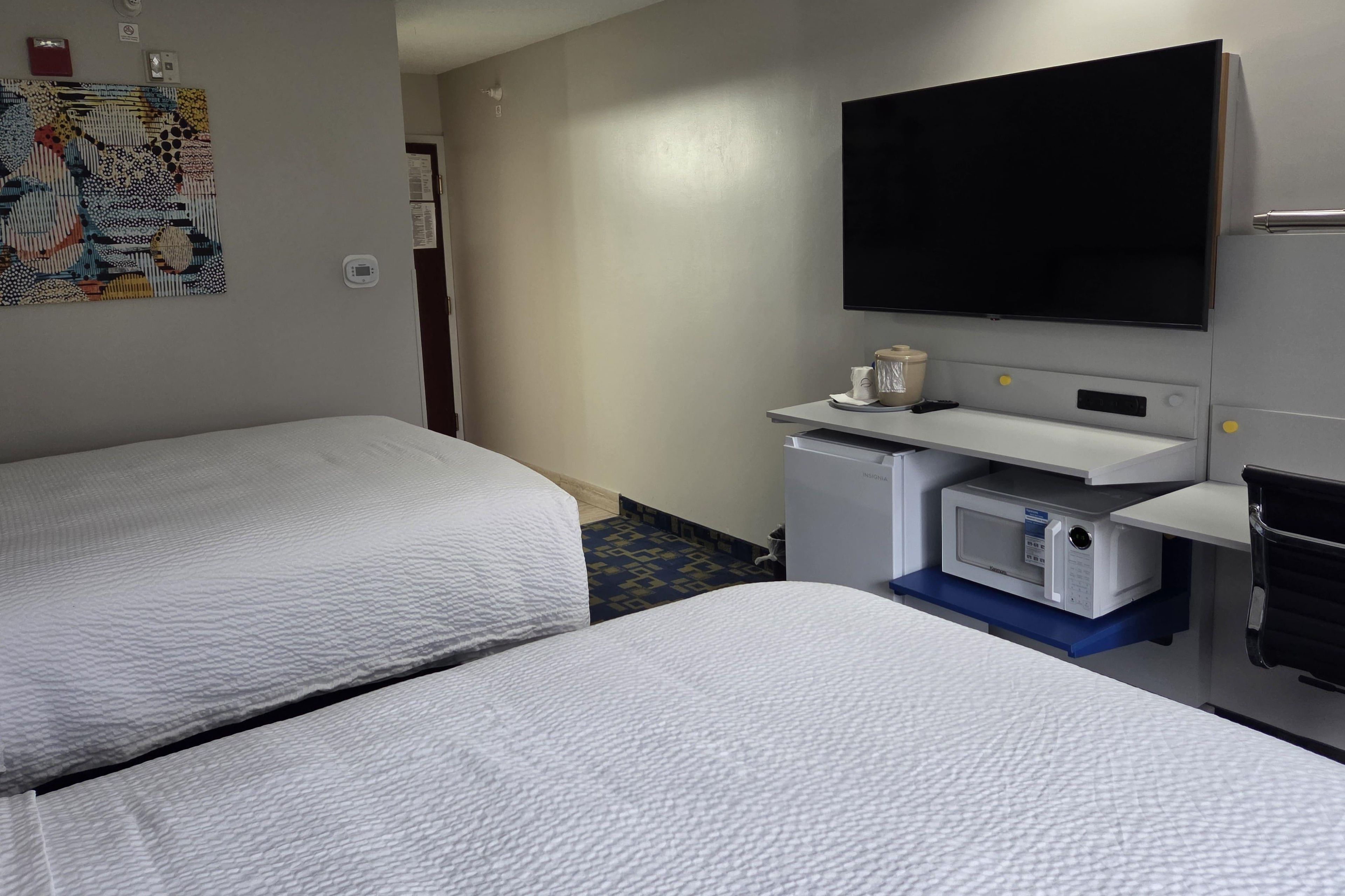 A hotel room with two beds, a flat-screen TV, a minibar, and a small desk.