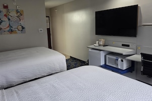 A hotel room with two beds, a flat-screen TV, a minibar, and a small desk.