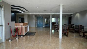 Un hall d’hôtel comprenant un comptoir d’accueil, des stanchions rouges et un espace détente avec des fauteuils.