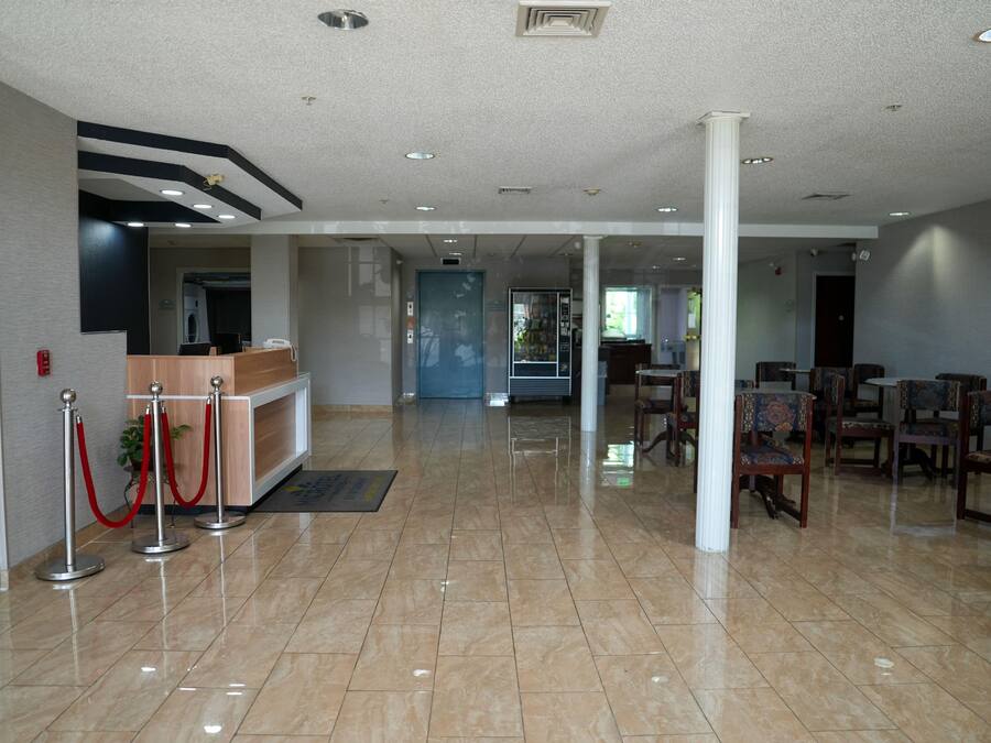 A hotel lobby with a reception desk, red stanchions, and a seating area with chairs.
