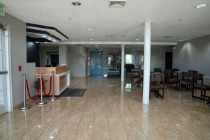 A hotel lobby with a reception desk, red stanchions, and a seating area with chairs.