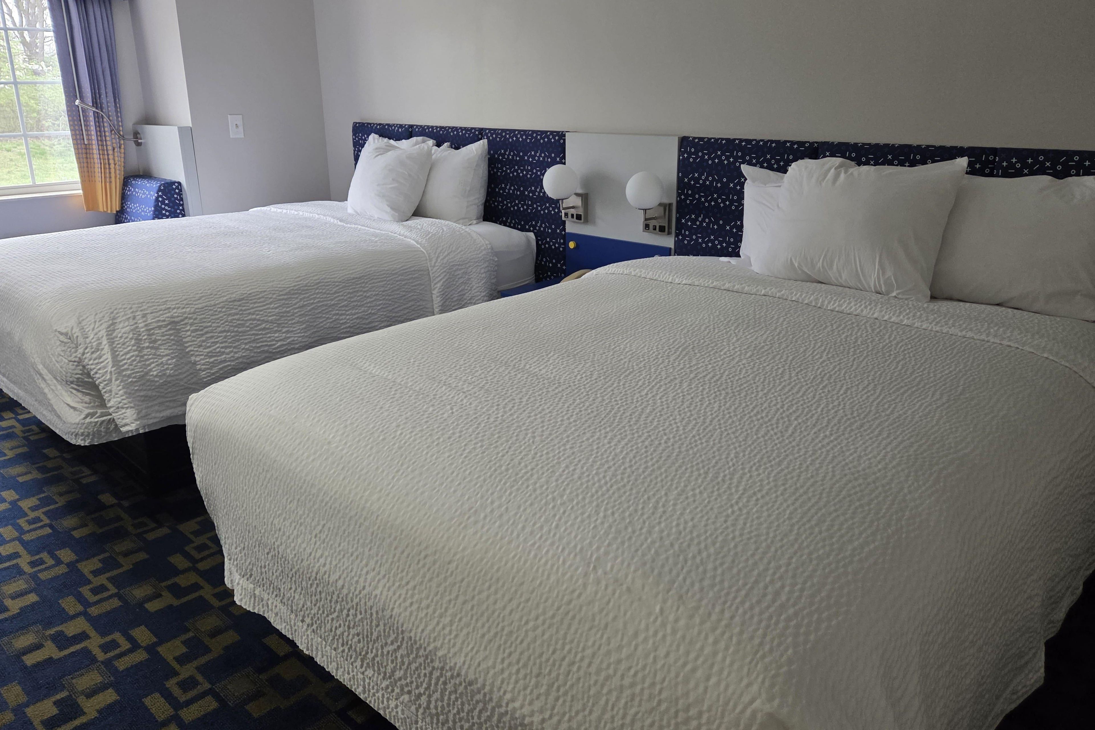 Habitación de hotel con dos camas, una alfombra estampada y una ventana con cortinas.