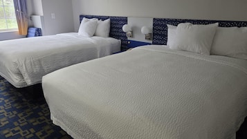 A hotel room with two beds, a patterned carpet, and a window with curtains.