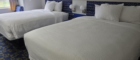 A hotel room with two beds, a patterned carpet, and a window with curtains.